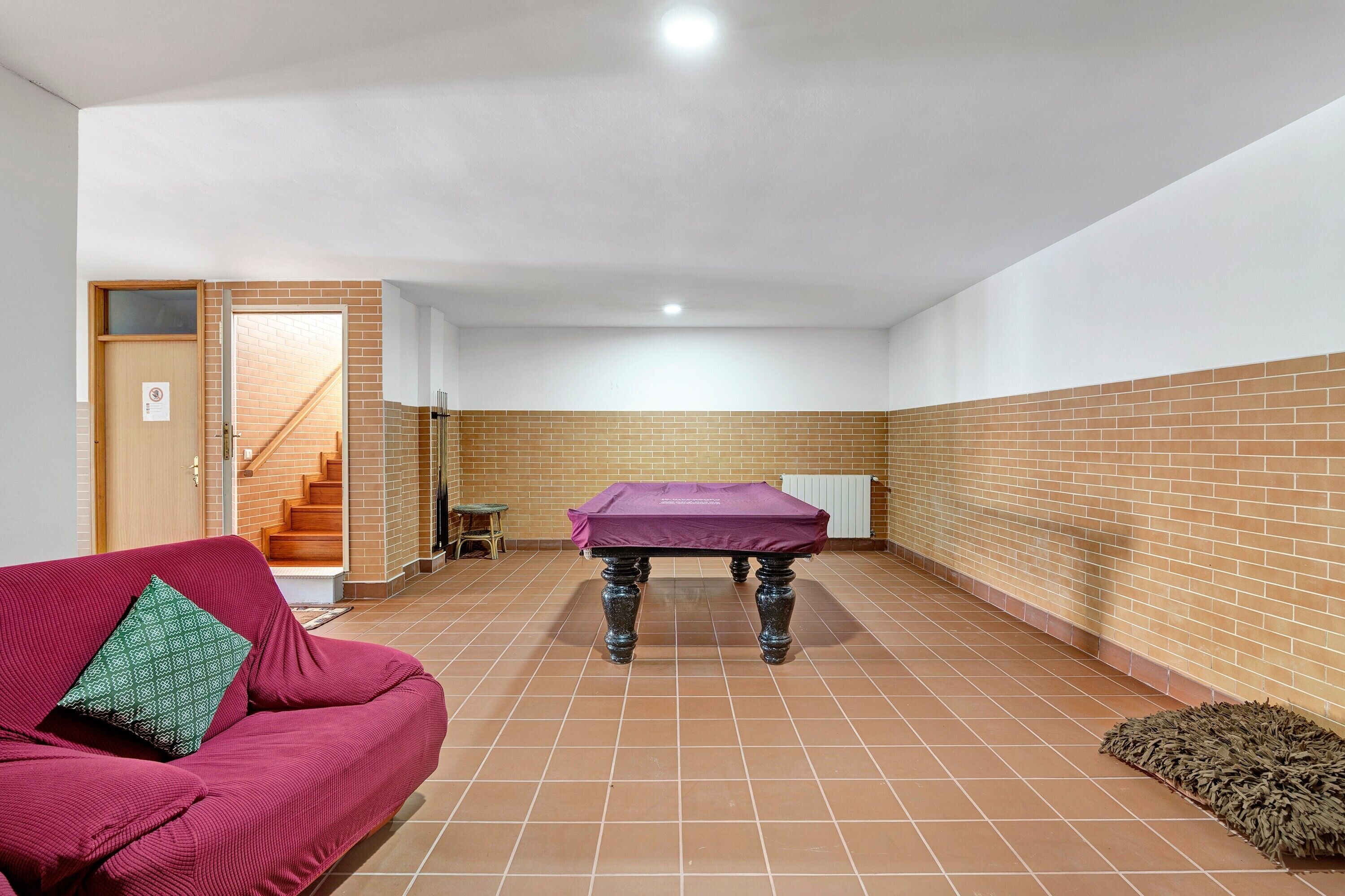 A room with a red sofa, a covered table, and a staircase leading to an upper floor.
