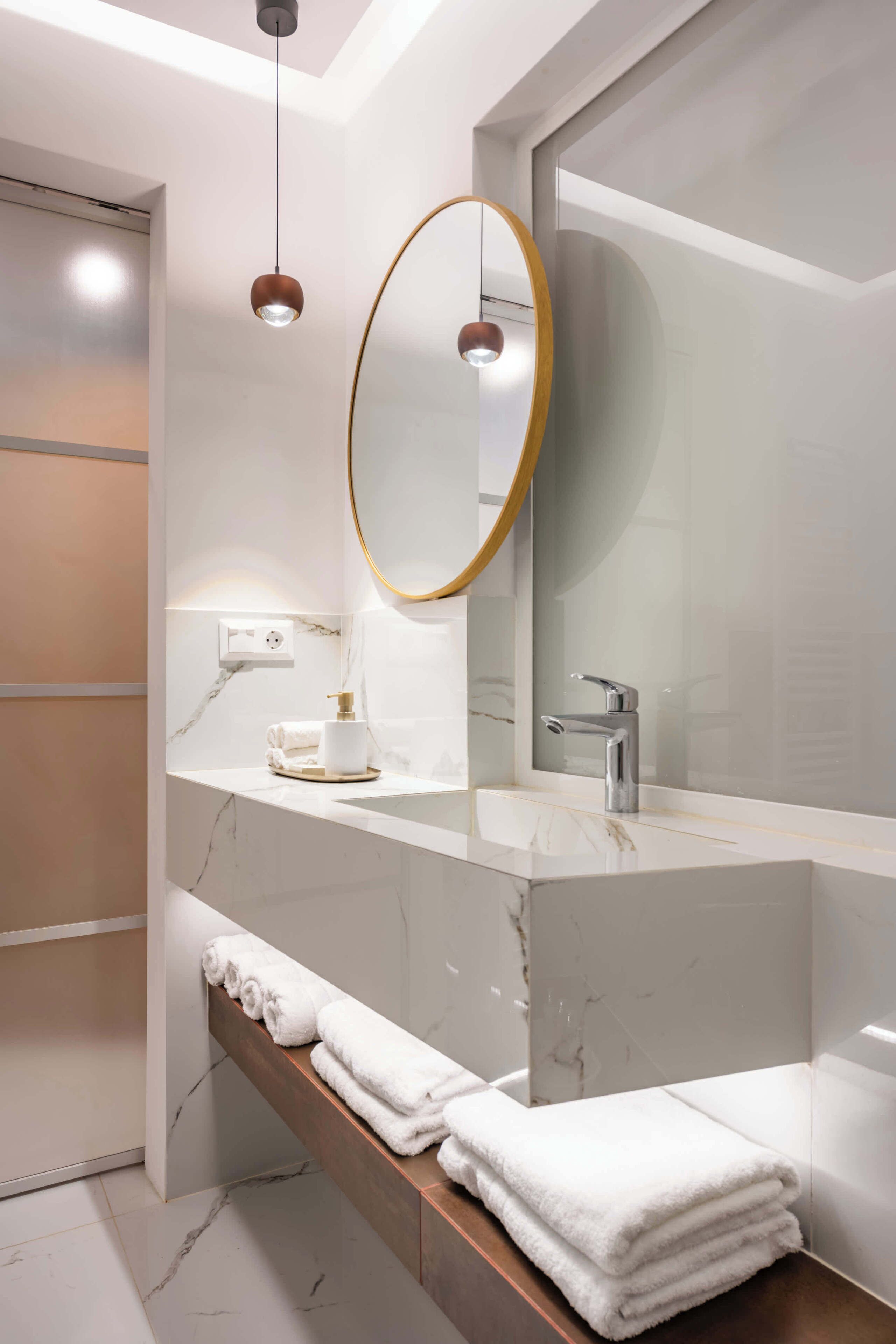 A modern bathroom with a marble vanity, a large mirror, a towel rack, and a built-in shower.