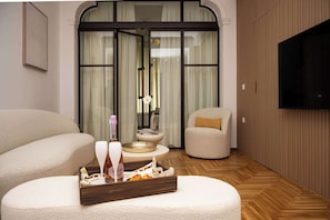 A modern living room with a sofa, a small table with a tray of snacks, a television, and a sliding glass door leading to a balcony. - Encore Living Residence - Athens Theater District (Athina)