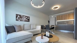 Een moderne woonkamer met een bank, een ronde salontafel en een eethoek met stoelen.