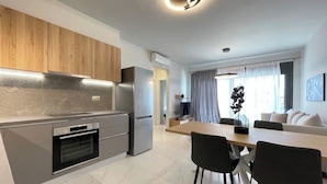 Een moderne keuken met een ingebouwde oven, een koelkast en houten kastjes. Er is een eethoek met een tafel en stoelen.