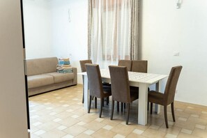 Uma área de refeições com uma mesa e cadeiras, um sofá com manta e uma janela com cortinas.