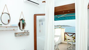 A bedroom with a bed, a bedside table, a mirror, and a view of the sea. - Triton Maisonette by RentalsPro (Fourka)