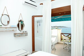 A bedroom with a bed, a bedside table, a mirror, and a view of the sea. - Triton Maisonette by RentalsPro (Fourka)