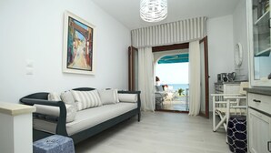 A modern living room with a sofa, a dining area, and a view of the sea. - Triton Maisonette by RentalsPro (Fourka)