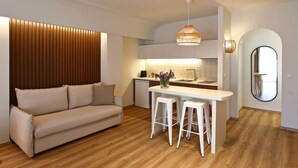Una cocina moderna con una isla central, un comedor con taburetes blancos, un sofá y suelo de madera.