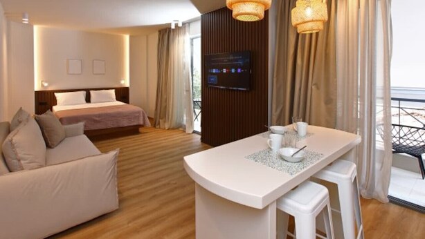 Een moderne hotelkamer met een bed, een zithoek met een sofa, een eettafel en een televisie.