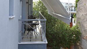 Een balkon met een tafel en stoelen, een witte luifel en uitzicht op groen en gebouwen.