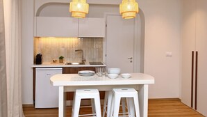 Een moderne keuken met witte kastjes, een inbouwvaatwasser, een wit aanrecht, twee witte krukken en twee hangende wilgenpendellampen.