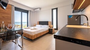 Ein modernes Hotelzimmer mit Bett, Schreibtisch mit Glasplatte, Küchenzeile und Meerblick.
