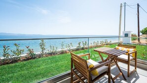 Ein Balkon mit Blick auf das Meer, Holzmöbel und eine Rasenfläche.
