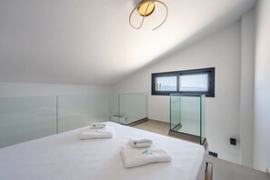 A modern bedroom with a glass partition, a bed with towels, a window, and a ceiling light fixture. - Azzurro e Verde Deluxe Suite 5 (Potidaia)