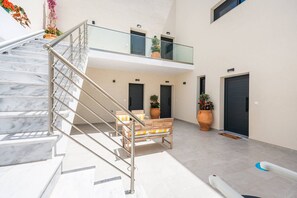 A modern building with a marble staircase, a second-floor balcony with glass railings, and a seating area with potted plants. - Azzurro e Verde Deluxe Suite 5 (Potidaia)