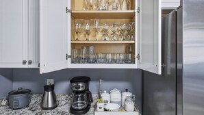 Ett kök med ett inbyggt skåp som innehåller olika typer av glasvaror och en kaffebryggare på bänkskivan.