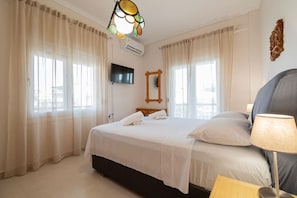 A hotel room with a bed, a TV, a mirror, and a lamp. - Thanos and Sofia by RentalsPro (Paralia Dionisiou)