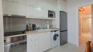 Una cocina compacta con armarios blancos, un microondas, un refrigerador, una lavadora y un lavaplatos.
