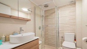 Un baño con ducha envuelta en vidrio, un lavamanos blanco y un inodoro.