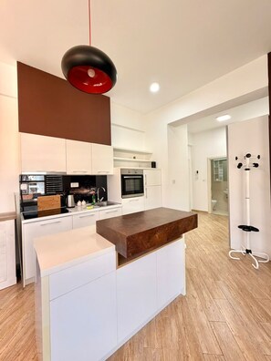 A modern kitchen with white cabinetry, a wooden countertop, and a hanging pendant light. - Orange Lux Apartments (Budva)