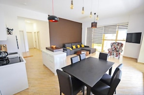 A modern living room with a sofa, dining table, and chairs. There is a kitchen area with a stove and cabinets. - Orange Lux Apartments (Budva)