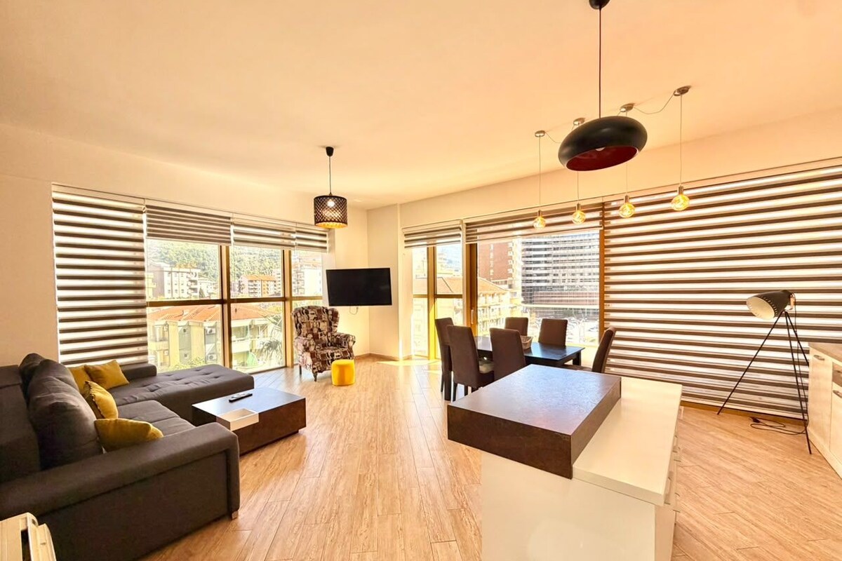 A modern living room with a sofa, a dining table, and a TV mounted on the wall.
