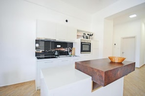 A modern kitchen with white cabinetry, a black stove, and a wooden countertop. - Orange Lux Apartments (Budva)