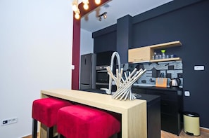 Una cocina moderna con encimera negra, un banco de madera con cojines rojos y un fregadero con utensilios colgando.