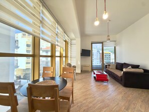 A modern living room with a round table, wooden chairs, a sofa, and a TV mounted on the wall. - Orange Lux Apartments (Budva)