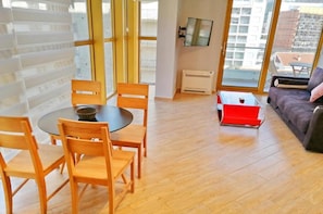 Una sala de estar moderna con una mesa redonda de madera, cuatro sillas, un sofá, una mesa de centro roja y un televisor montado en la pared.
