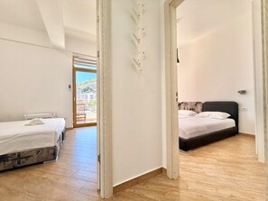 A room with two beds, a wooden floor, and a view through an open door to an outdoor area. - Orange Lux Apartments (Budva)