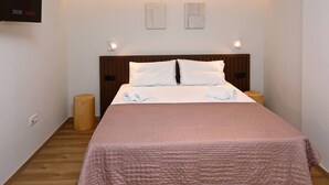 A neatly made bed with a pink bedspread, two bedside tables, and a wall-mounted TV. - Local Suite 3 - Nea Moudania (Nea Moudania)