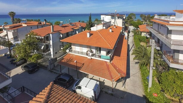 Uma área residencial costeira com edifícios de telhado em terracota, céu azul límpido e vista para o mar.