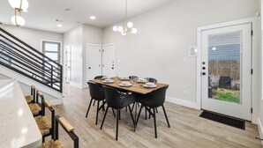 A dining area with a wooden table, black chairs, and a staircase with black railings. - SA Modern Home Nr River Walk + DT | BBQ Yard Games (San Antonio)