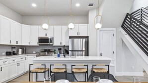 A modern kitchen with white cabinets, a central island, and a dining area with four chairs. - SA Modern Home Nr River Walk + DT | BBQ Yard Games (San Antonio)