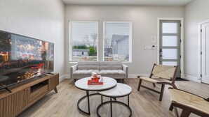 A living room with a TV, sofa, two tables, and a chair. - SA Modern Home Nr River Walk + DT | BBQ Yard Games (San Antonio)