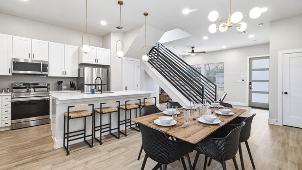 A modern kitchen with stainless steel appliances, a wooden dining table, black chairs, and a staircase. - SA Modern Home Nr River Walk + DT | BBQ Yard Games (San Antonio)