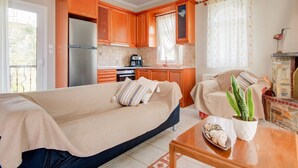 A compact living space with a sofa, a dining table, a kitchen area, and a fireplace. - Azure Bay Villa by RentalsPro (Neos Marmaras)