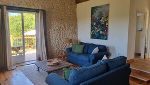 Una sala de estar con pared de piedra, un sofá azul, una mesa de centro de madera y un cuadro de flores.