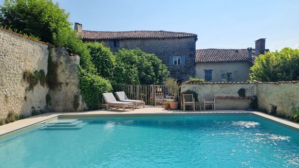 Una piscina con sillas de descanso, un muro de piedra y un edificio con tejado de baldosas.