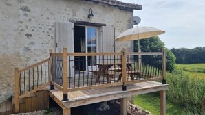 Un edificio rústico con una terraza de madera, una mesa y sillas, y una puerta abierta.
