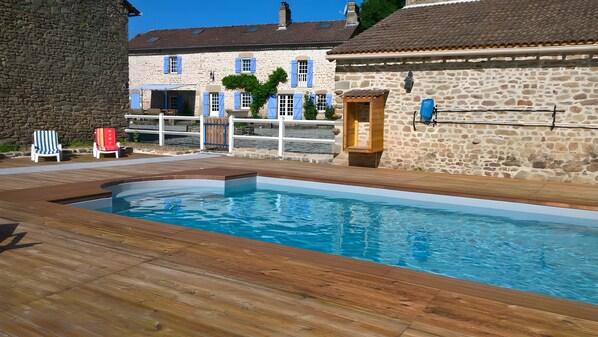 A swimming pool with a wooden deck, stone buildings, and outdoor seating. - Le Gîte D'Au: Heated Pool, Spa & Fishing Pond (Saint-Amand-Magnazeix)