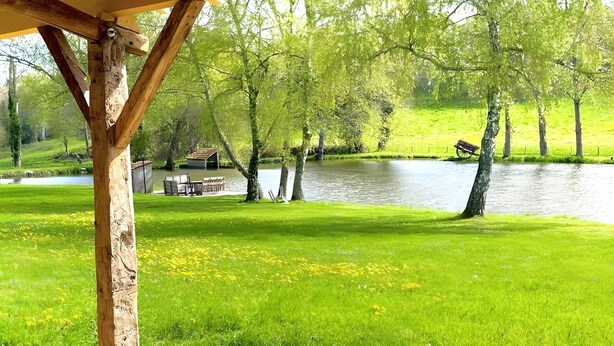 A hot tub with a wooden pergola overhead, surrounded by a grassy area and a body of water. - Le Gîte D'Au: Heated Pool, Spa & Fishing Pond (Saint-Amand-Magnazeix)