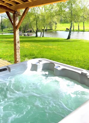 A hot tub with a wooden pergola overhead, surrounded by a grassy area and a body of water. - Le Gîte D'Au: Heated Pool, Spa & Fishing Pond (Saint-Amand-Magnazeix)