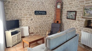 A living room with a stone wall, a sofa, a wooden coffee table, a television, a clock, and a framed picture. - Le Gîte D'Au: Heated Pool, Spa & Fishing Pond (Saint-Amand-Magnazeix)