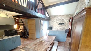 A rustic kitchen with a wooden table, a staircase, and a stone wall with a sign. - Le Gîte D'Au: Heated Pool, Spa & Fishing Pond (Saint-Amand-Magnazeix)