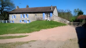 A stone building with a sloped roof, a dirt driveway, and a grassy area. - Le Gîte D'Au: Heated Pool, Spa & Fishing Pond (Saint-Amand-Magnazeix)