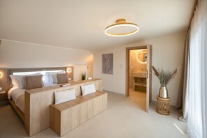 A modern hotel room with a large bed, a seating area, a bathroom with a mirror, and a vase with pampas grass.