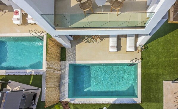 A rooftop pool area with two separate pools, lounge chairs, and a glass balustrade.