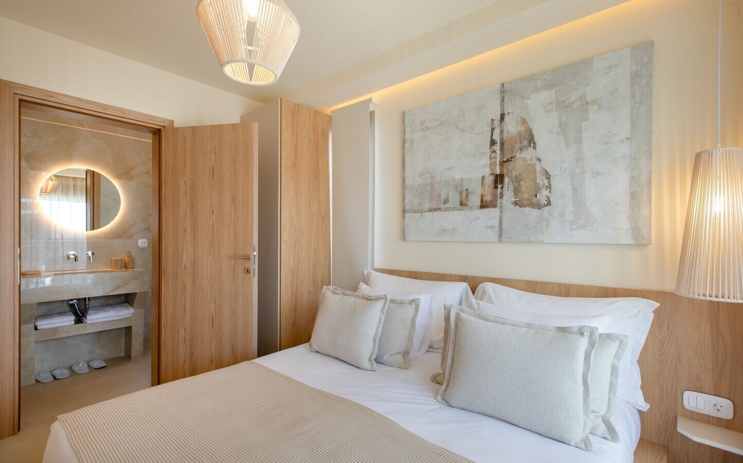 Une chambre moderne avec un grand lit, une armoire intégrée, un miroir rond et une œuvre d’art accrochée au mur.