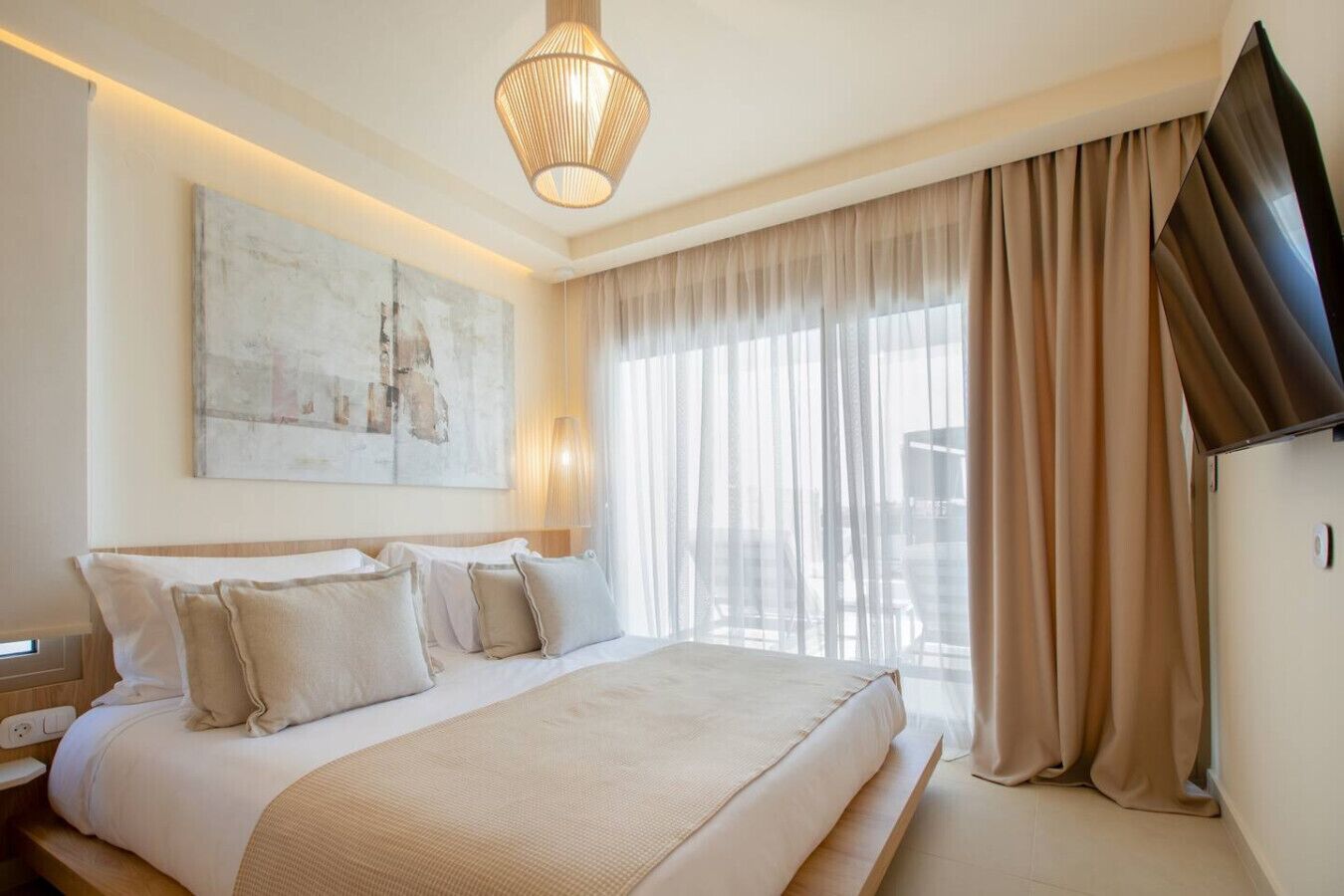 Ett hotellrum med en stor säng, en platt-TV, en tavla på väggen och ett fönster med gardiner.