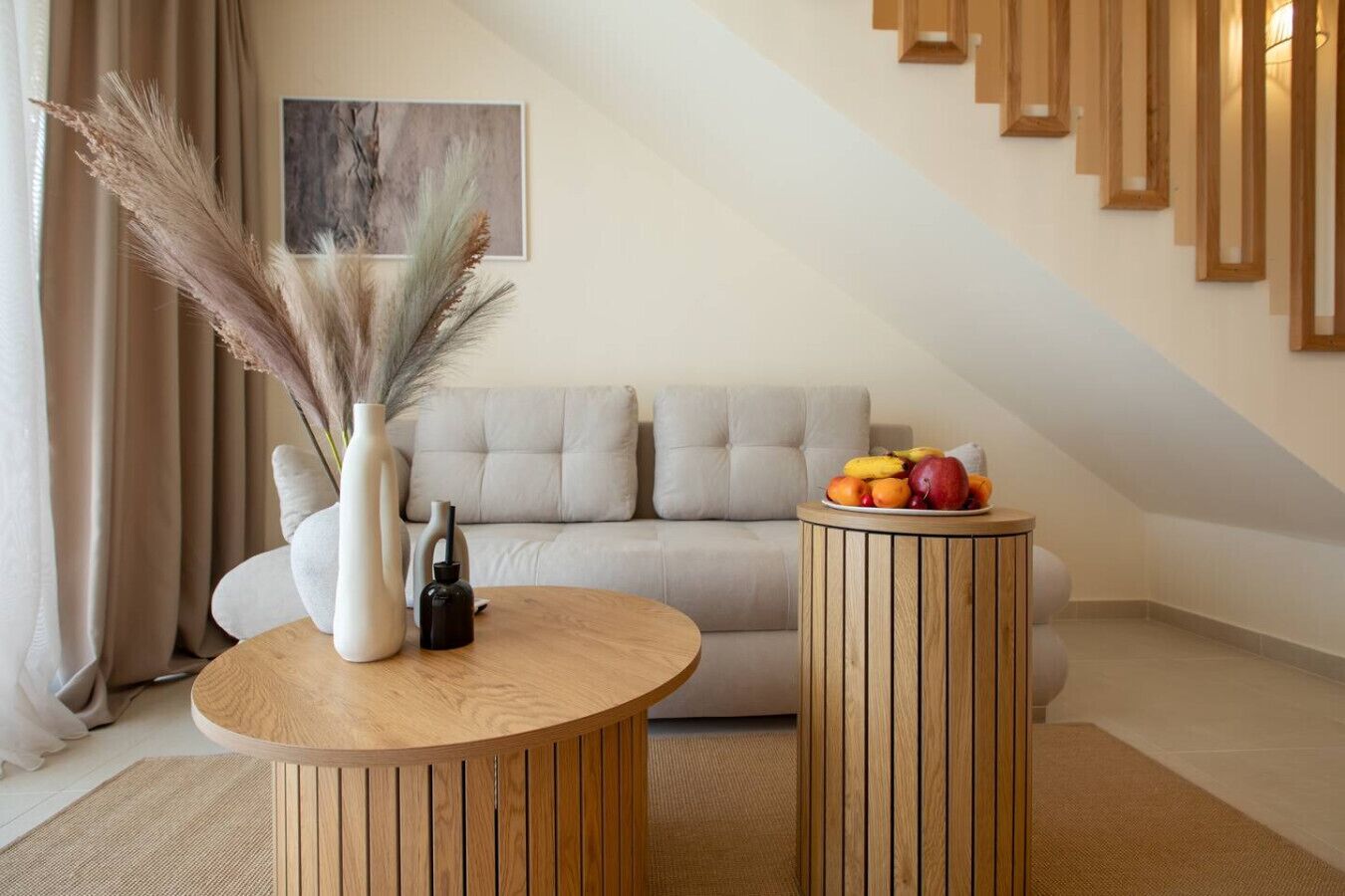 Un salon moderne avec un canapé, une table ronde en bois sur laquelle sont posés un vase et une bouteille, ainsi qu’un panier de fruits.